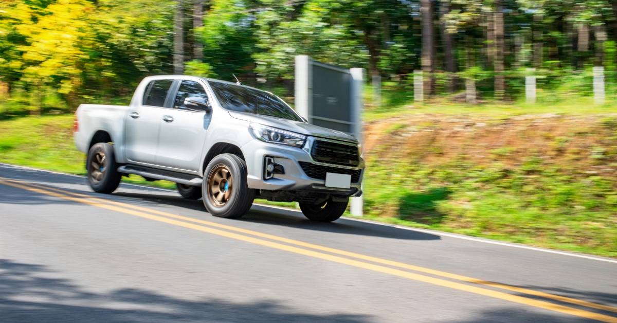 A silver pickup truck is driving fast down the road with the background of trees and telephone wires blurring.